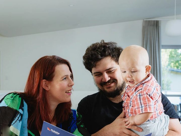 A couple holding their baby with a blue Pukeko management folder open in front of them.